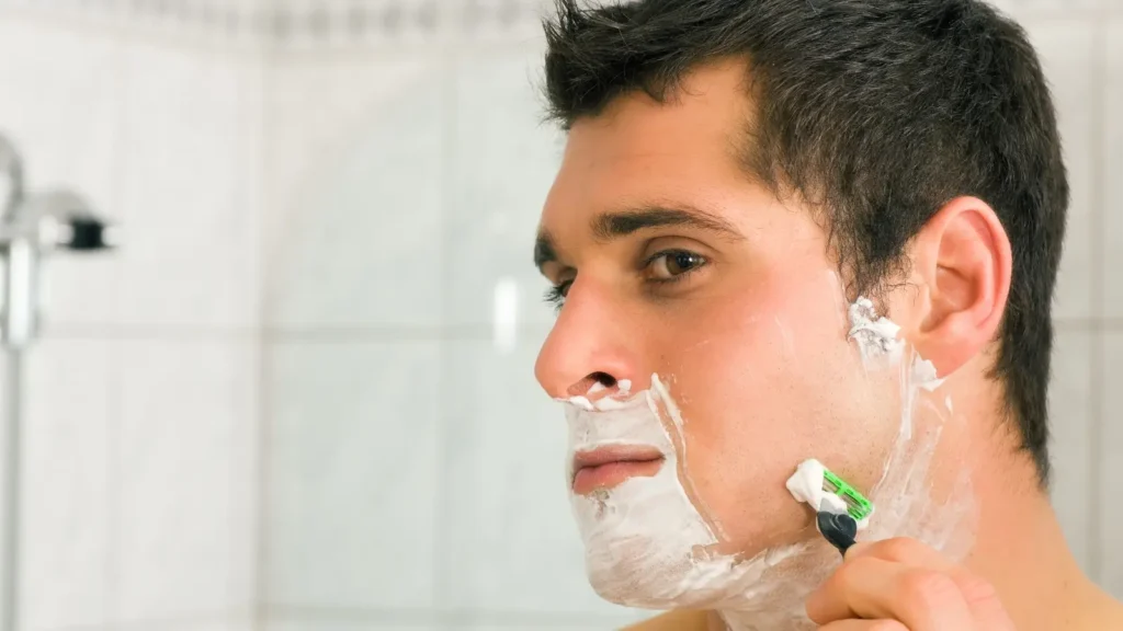 Uomo applica schiuma da barba davanti allo specchio.