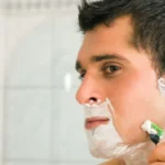 Uomo applica schiuma da barba davanti allo specchio.